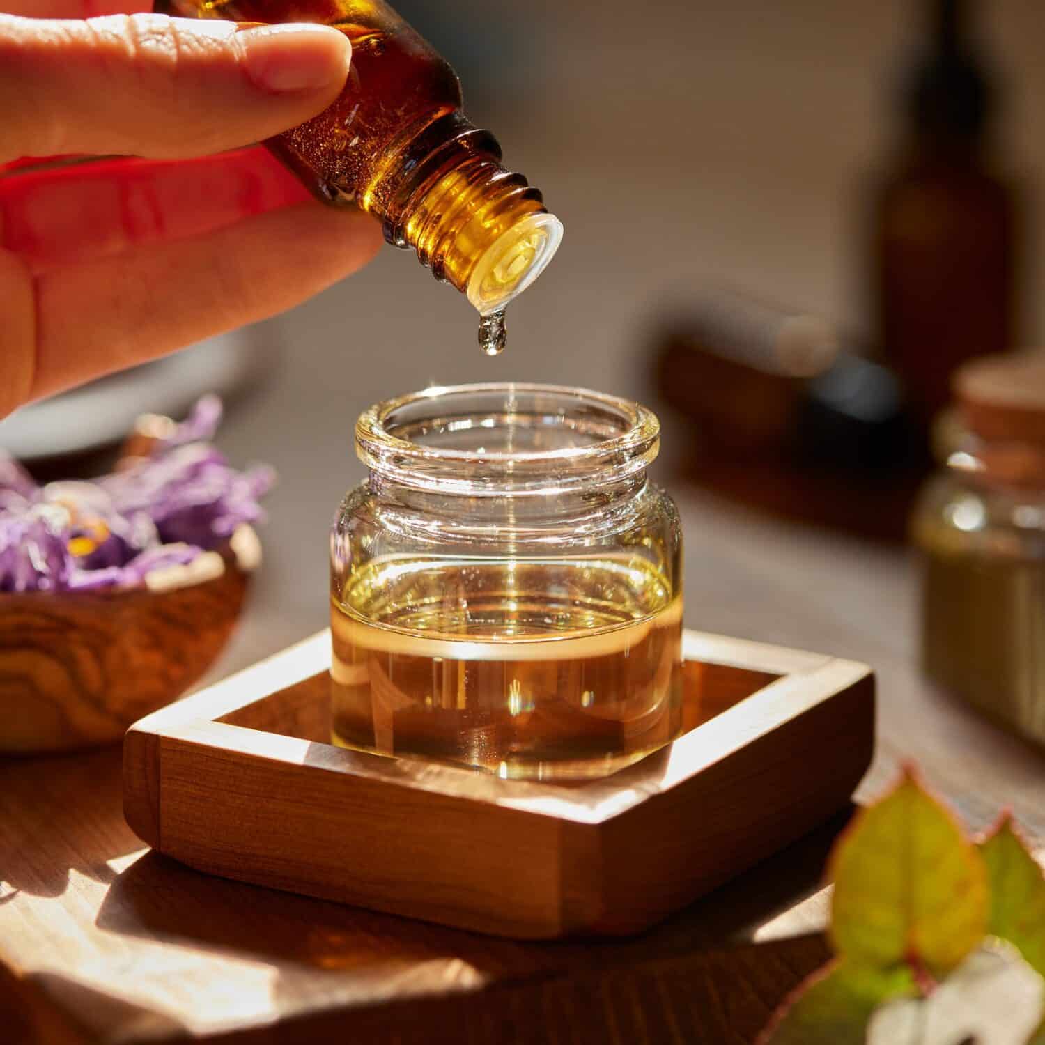 Essential oil dropper over a glass jar on a wooden tray.