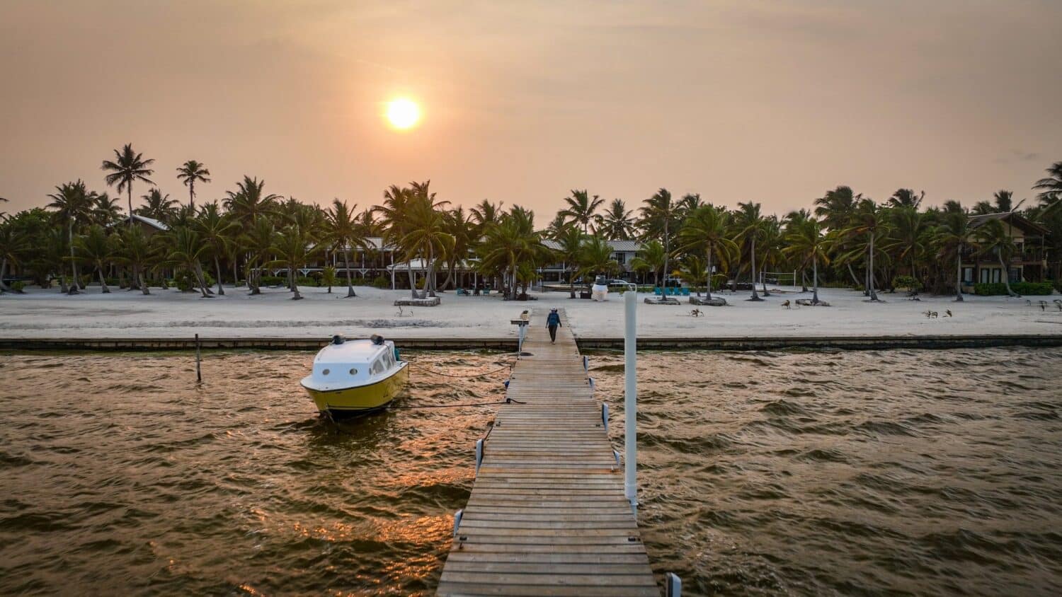 Serene golden sunset over El Pescador Beach Resort with palm trees and a docked boat.