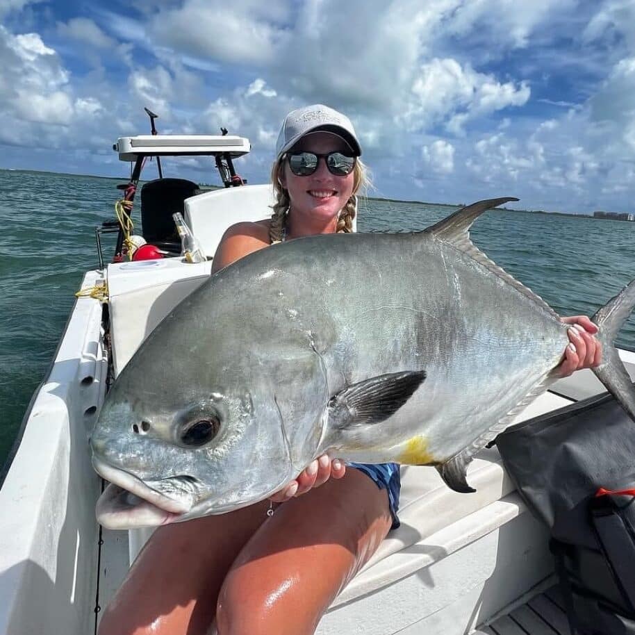 Woman proudly holding a large fish on a sunny fishing adventure.