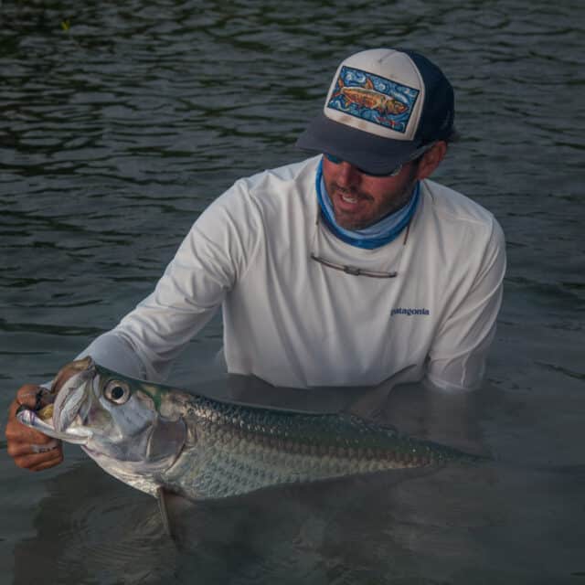 http://Fisherman%20proudly%20displays%20a%20tarpon%20catch%20in%20tranquil%20water.