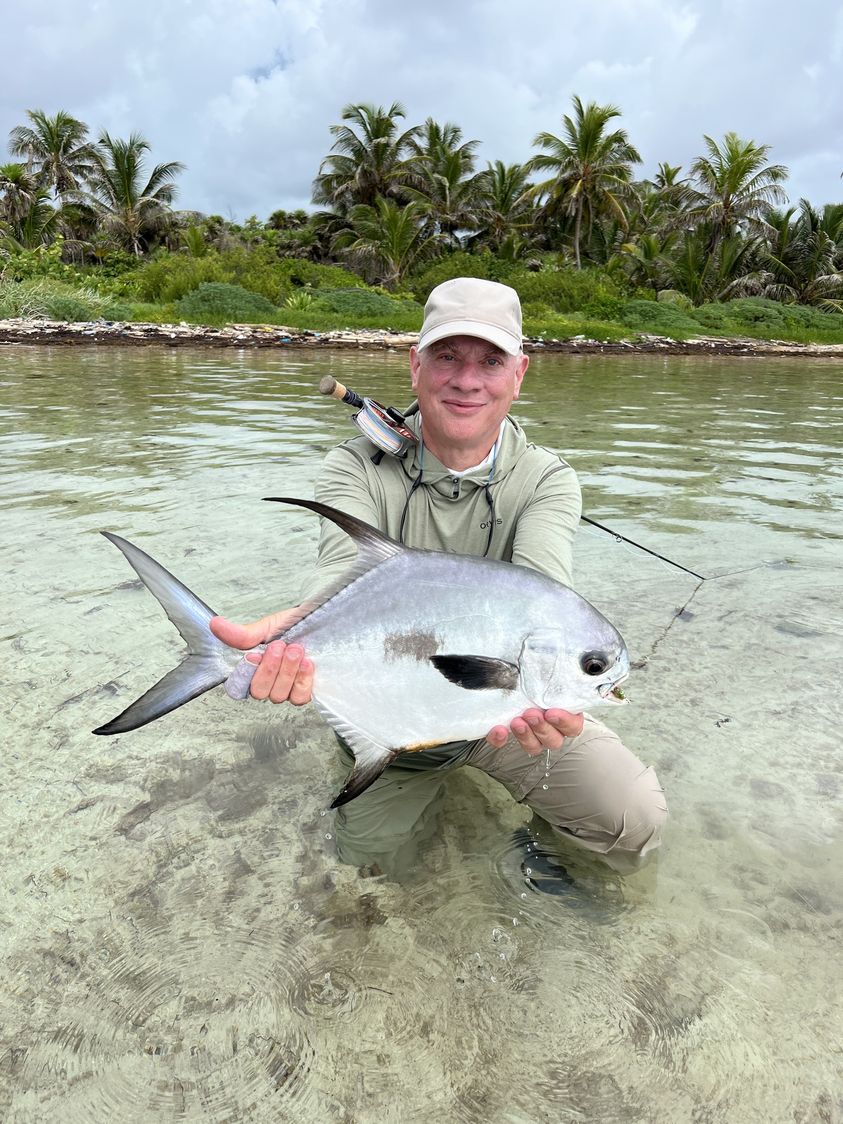 Angler proudly displaying a caught fish in serene waters surrounded by palm trees.