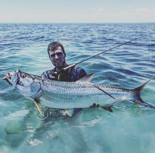 Angler proudly holds a large tarpon in clear waters during a fishing adventure.