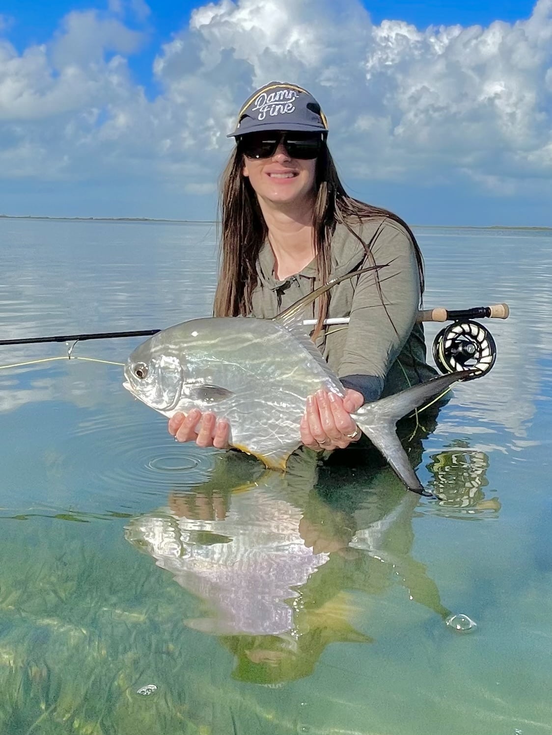 Angler proudly holds a beautiful fish in serene, clear waters under a bright sky.