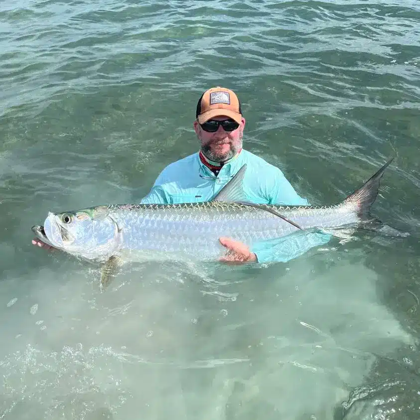 Angler proudly holding a large tarpon in clear waters during fishing trip.