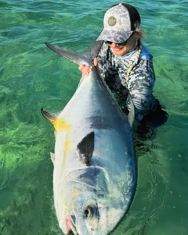 Woman catches a large fish in crystal-clear water during an exciting fishing adventure.