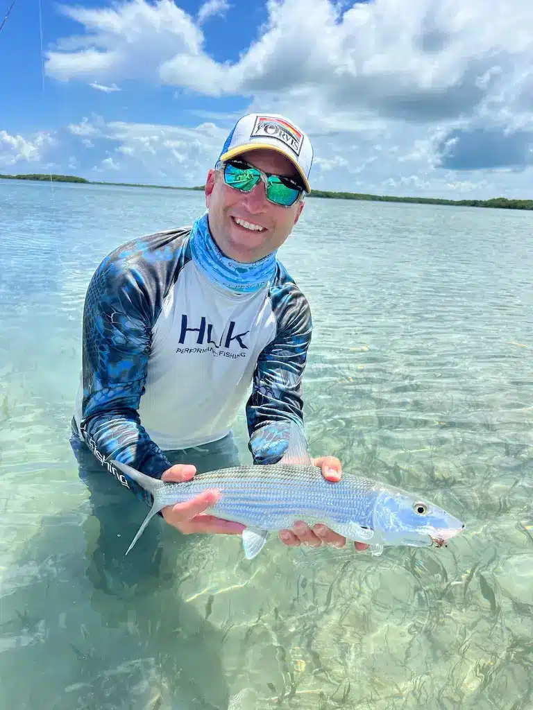 Angler proudly holding a fish in crystal clear water under a bright blue sky.