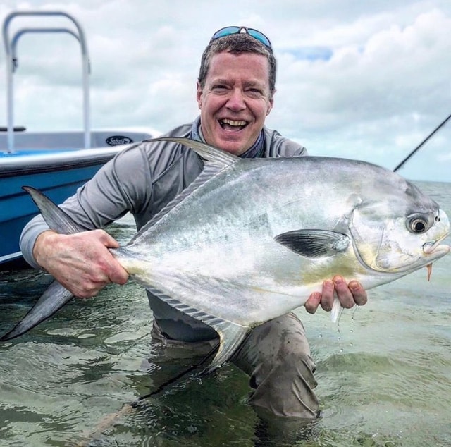 Joyful angler beaming while holding his large catch in shallow water.