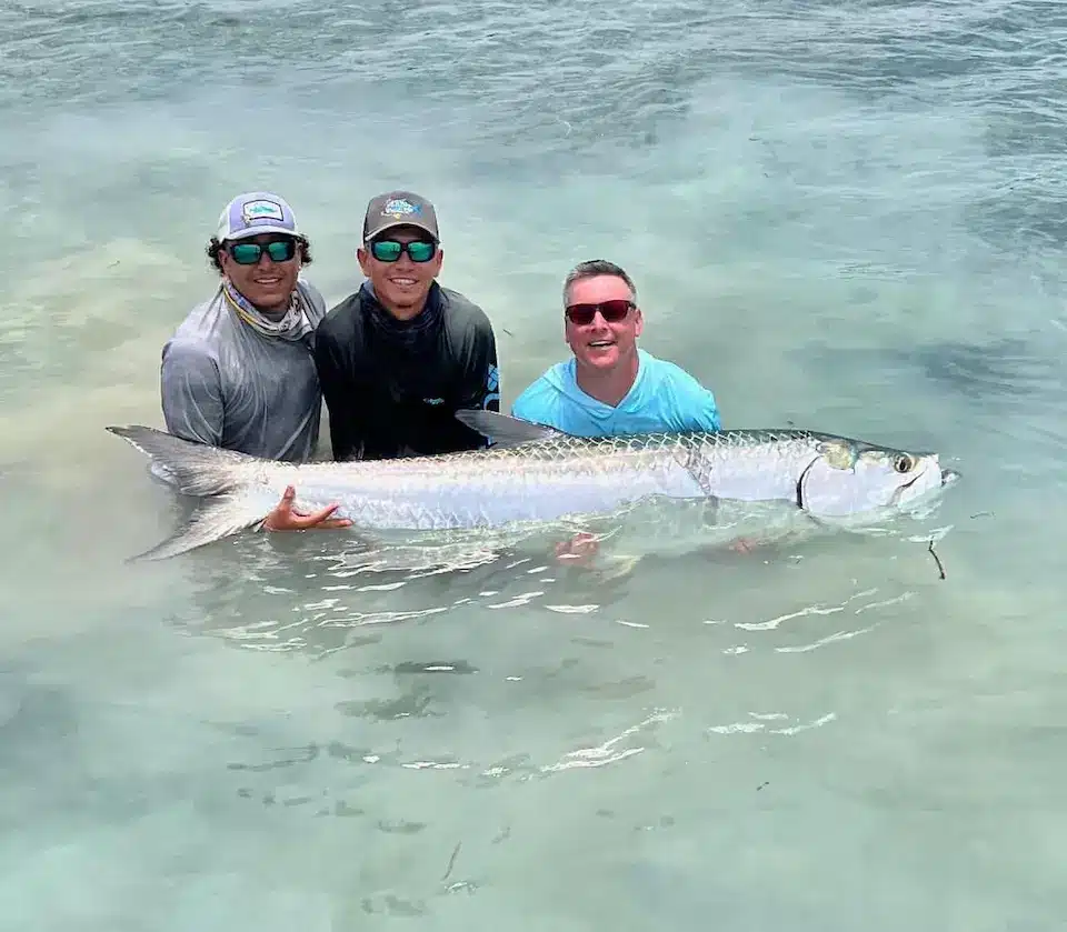 Three anglers celebrate a successful tarpon fishing trip in crystal-clear waters.